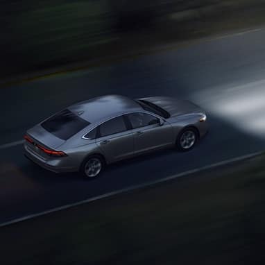 High angled 3/4 rear passenger shot of the 2026 Honda Accord driving on an open road at night.