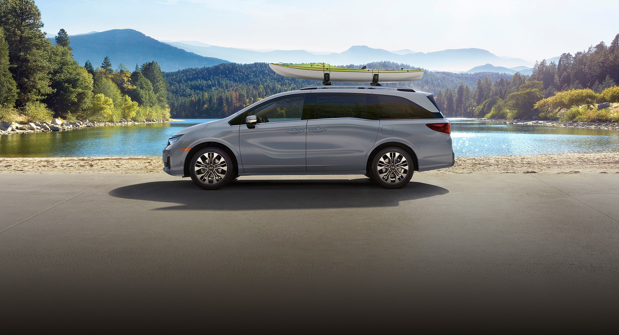2027 Honda Odyssey Elite in Sonic Gray Pearl profile parked by a lake with a kayak on the roof (Minivan).